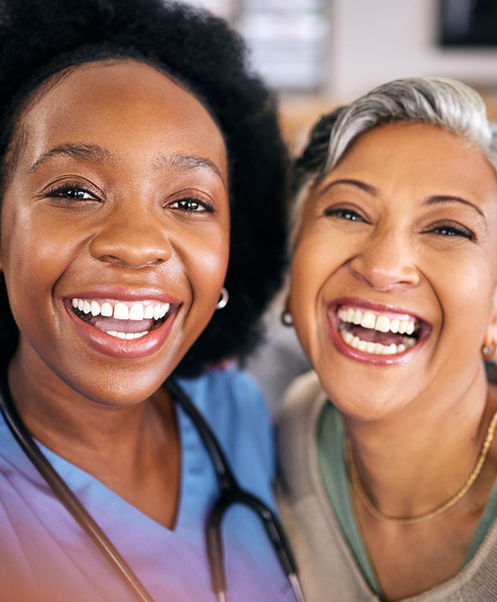 Two women smiling together, one in medical scrubs.