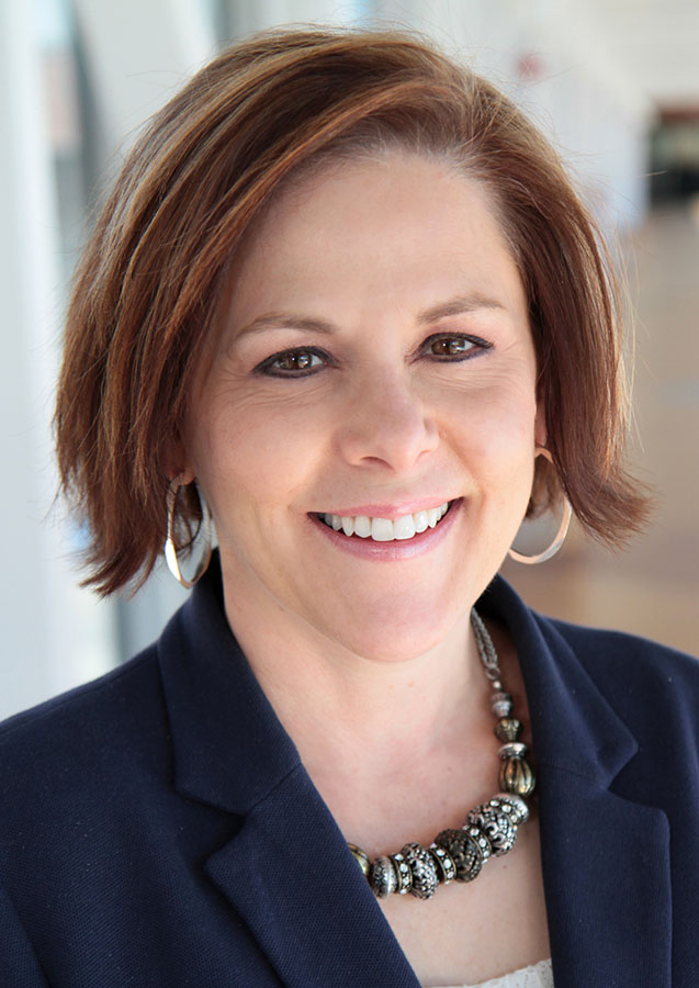 Smiling person with short brown hair and necklace.