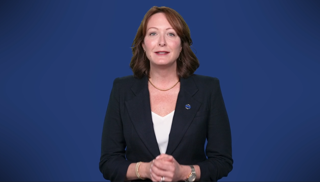 Person in business attire speaking on blue background.