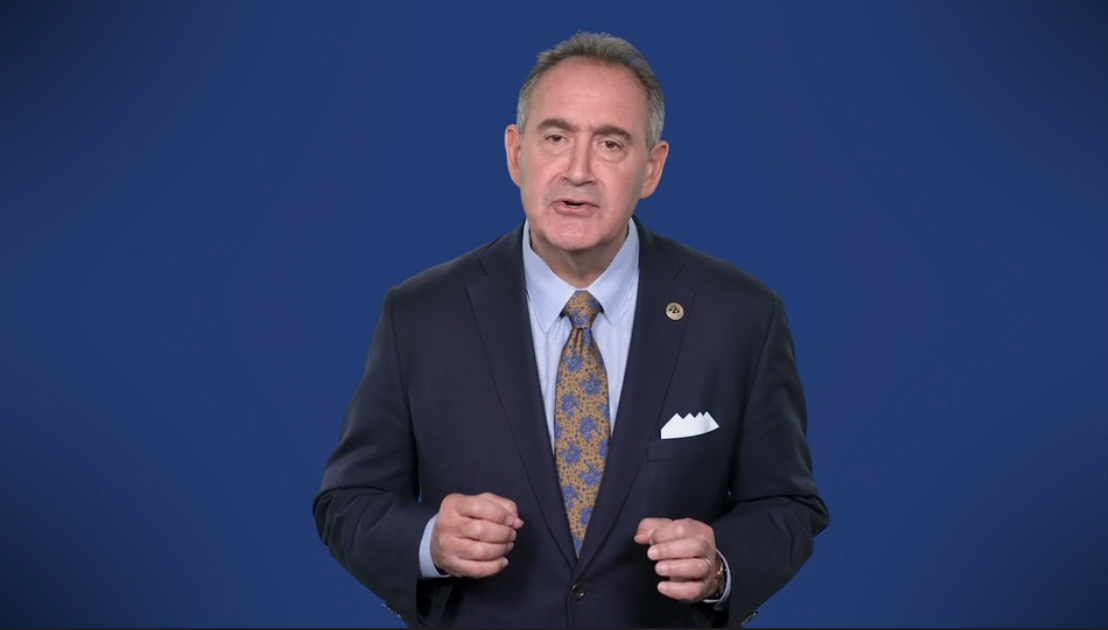 Man in suit giving speech against blue background.